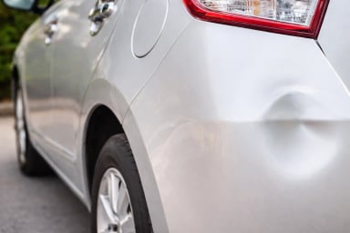 Close-up of a dented silver car rear panel