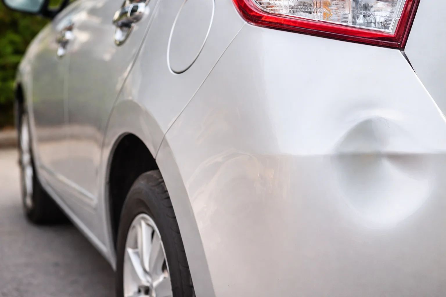 Close-up of a dented silver car rear panel