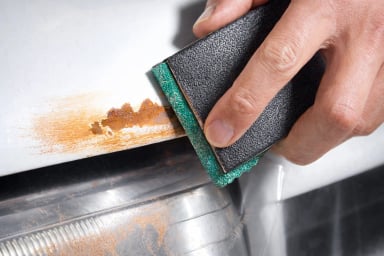 Person removing rust from a car body with a sanding block